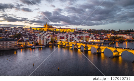 Prague Castle stands on the hill while Charles Bridge stretches over the Vltava River. The city lights glow as dusk settles, creating a scenic view of Czechia. Prague Castle stands on the hill while Charles Bridge stretches over the Vltava River. The city lights glow as dusk settles, creating a scenic view of Czechia. 137050755