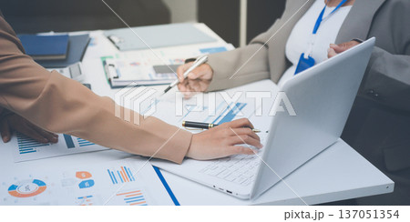 Business colleagues analyzing financial charts and reports on the table while having a focused discussion about strategies and market performance during an important meeting in a modern office setup Business colleagues analyzing financial charts and reports on the table while having a focused discussion about strategies and market performance during an important meeting in a modern office setup 137051354