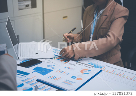 Business colleagues analyzing financial charts and reports on the table while having a focused discussion about strategies and market performance during an important meeting in a modern office setup 137051372