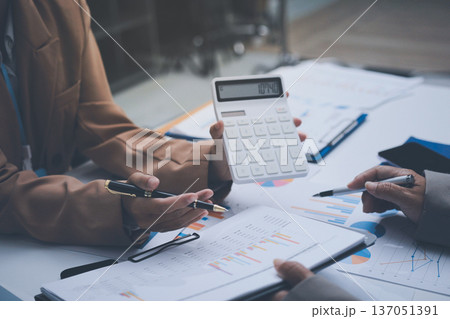 Business colleagues analyzing financial charts and reports on the table while having a focused discussion about strategies and market performance during an important meeting in a modern office setup 137051391