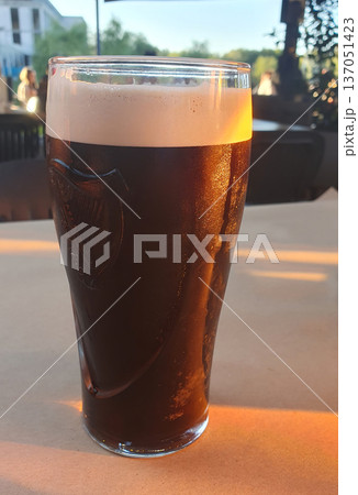 A refreshing glass of dark beer with thick foam stands on the table on a hot summer day A refreshing glass of dark beer with thick foam stands on the table on a hot summer day 137051423