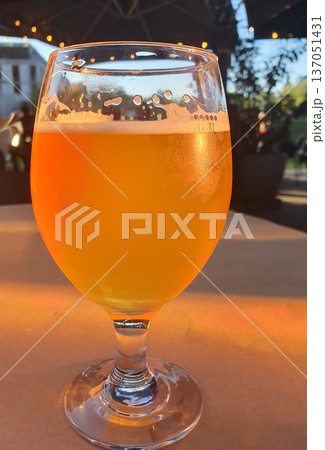 A refreshing glass of light beer with a thick, snow-white head stands on a table under the scorching summer sun 137051431
