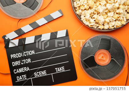 Movie clapper with popcorn and film reels on orange background 137051755