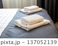 Folded white towels on hotel bed close up with clean modern hospitality interior 137052139