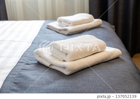 Folded white towels on hotel bed close up with clean modern hospitality interior 137052139