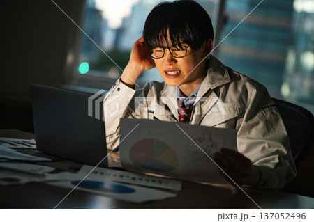 仕事が終わらず夜遅くまで残業をする若いビジネスマン 137052496