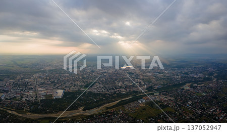 Aerial view from high altitude of distant city covered with puffy cumulus clouds flying by before rainstorm at sunset. Airplane point of view of landscape in cloudy weather Aerial view from high altitude of distant city covered with puffy cumulus clouds flying by before rainstorm at sunset. Airplane point of view of landscape in cloudy weather 137052947