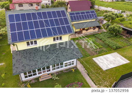 Aerial top view of new modern residential house cottage with blue shiny solar photo voltaic panels system on roof. Renewable ecological green energy production concept. Aerial top view of new modern residential house cottage with blue shiny solar photo voltaic panels system on roof. Renewable ecological green energy production concept. 137052956