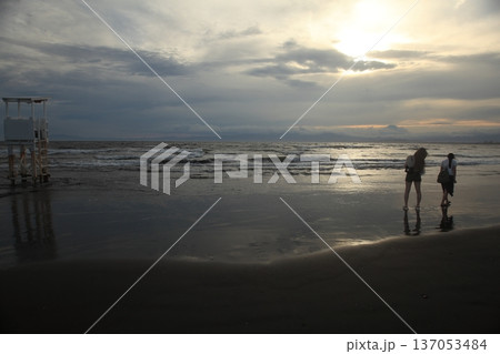 夕暮れの海岸を歩く人 137053484