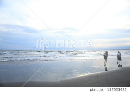 夕暮れの海岸を歩く人 137053485