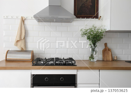 Modern eclectic kitchen interior. White metro tiles wall background. Old oil painting. Wooden countertop, stainless steel hood and gas stove. Scandinavian design. Home staging. Vase of cow parsley Modern eclectic kitchen interior. White metro tiles wall background. Old oil painting. Wooden countertop, stainless steel hood and gas stove. Scandinavian design. Home staging. Vase of cow parsley 137053625