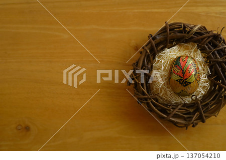 木製テーブルの上に置かれた鳥の巣の中の伝統的な麦わら細工のイースターエッグのコピースペースがある写真 137054210