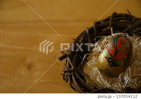 木製テーブルの上に置かれた鳥の巣の中の伝統的な麦わら細工のイースターエッグのコピースペースがある写真 137054212