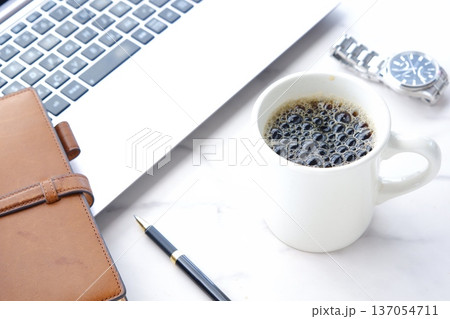 淹れたての美味しいコーヒーを飲みながら、ノートパソコンとシステム手帳でデスクワークをしているイメージ 淹れたての美味しいコーヒーを飲みながら、ノートパソコンとシステム手帳でデスクワークをしているイメージ 137054711