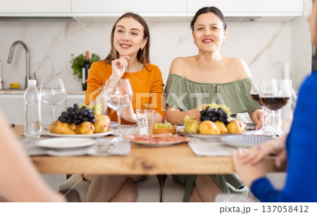 Four women are sitting at table, enjoying food and wine, chatting, talking, laughing. Four women are sitting at table, enjoying food and wine, chatting, talking, laughing. 137058412