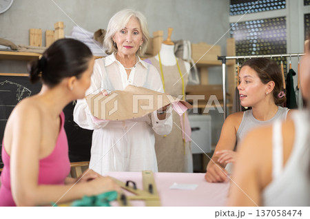 Female teacher explaining pattern structure by chalkboard during sewing course for adults Female teacher explaining pattern structure by chalkboard during sewing course for adults 137058474