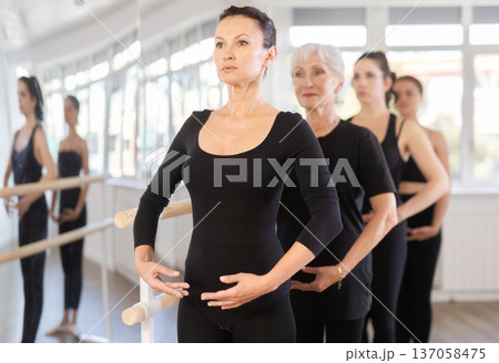 Graceful women doing ballet on ballet barre in training room during training, standing in fifth position near ballet barre Graceful women doing ballet on ballet barre in training room during training, standing in fifth position near ballet barre 137058475