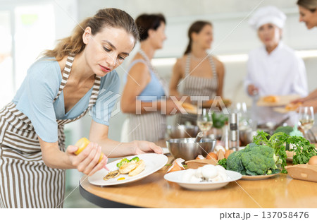 Girl visitors to culinary school decorates finished dish, fried chicken fillet with golden crust. Girl visitors to culinary school decorates finished dish, fried chicken fillet with golden crust. 137058476