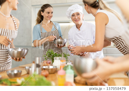 Elderly woman chef with bowl in hands tells women at culinary courses about traditions of cuisine Elderly woman chef with bowl in hands tells women at culinary courses about traditions of cuisine 137058479