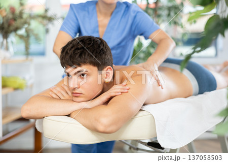 Female masseur doing massage at back man who lying on massage table in beauty salon 137058503