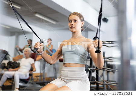 Athletic woman working on special machine with ropes to develop arm muscles Athletic woman working on special machine with ropes to develop arm muscles 137058521