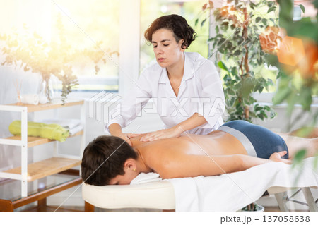 Adult woman giving back massage to young guy Adult woman giving back massage to young guy 137058638