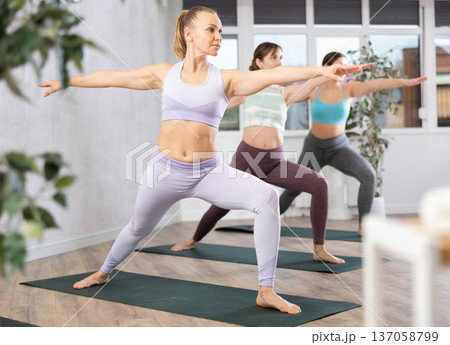 Diligent women practicing warrior pose of yoga in light fitness room 137058799