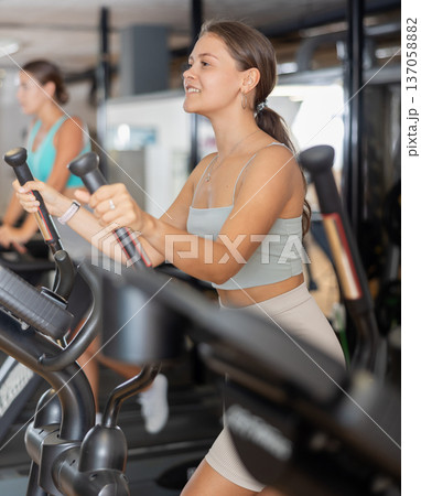 Slender athletic girl during cardio exercises on elliptical simulator in fitness center. Slender athletic girl during cardio exercises on elliptical simulator in fitness center. 137058882