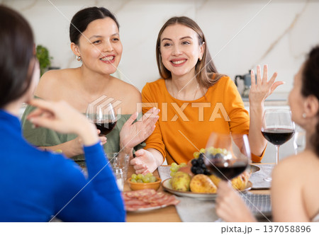 Four women are sitting at table, enjoying food and wine, chatting, talking, laughing. 137058896