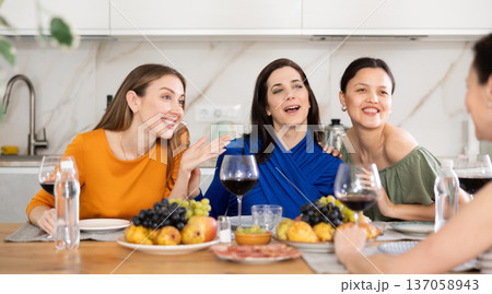 Girlfriends drinking wine and having conversation over dinner at house party Girlfriends drinking wine and having conversation over dinner at house party 137058943