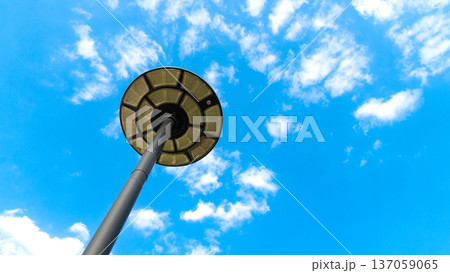 Bottom view looks up at the lamppost with its solar-powered light fixture. Under blue sky and white clouds. 137059065
