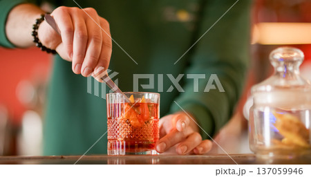 Garnishing cocktail. Alcoholic mix. Barman preparing refreshing drink with ice cube. Cold negroni served with orange fruit zest in glass. Garnishing cocktail. Alcoholic mix. Barman preparing refreshing drink with ice cube. Cold negroni served with orange fruit zest in glass. 137059946