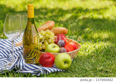 Picnic with wine, fruits, and baguette on a green meadow 137060882