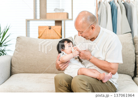 抱っこして哺乳瓶で孫にミルクをあげる笑顔の祖父,おじいちゃん 抱っこして哺乳瓶で孫にミルクをあげる笑顔の祖父,おじいちゃん 137061964