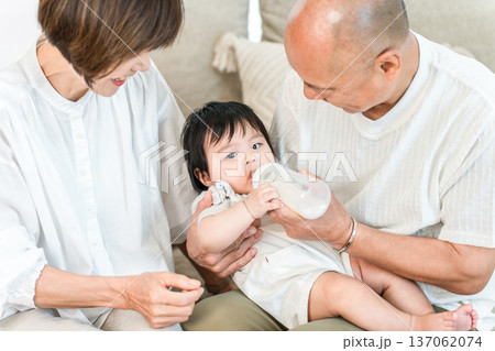 抱っこして哺乳瓶で孫にミルクをあげる笑顔のおじいちゃんとおばあちゃん 137062074