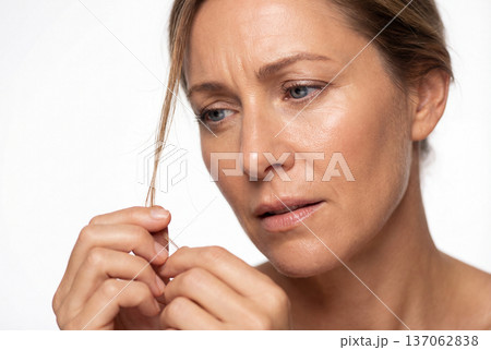 Middle aged woman examining hair strand with worried expression 137062838