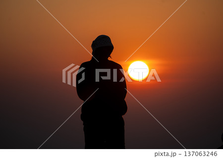 Silhouette of people camping with an orange tent on a high mountain peak enjoying a spectacular glowing sunrise. Silhouette of people camping with an orange tent on a high mountain peak enjoying a spectacular glowing sunrise. 137063246