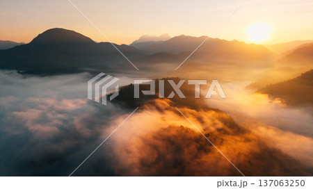 Breathtaking aerial view of golden sunlight hitting a sea of fog flowing through mountain ridges at sunrise. Breathtaking aerial view of golden sunlight hitting a sea of fog flowing through mountain ridges at sunrise. 137063250