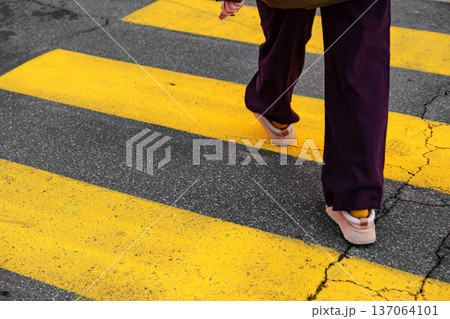 Person walks on yellow crosswalk lines in urban area on a clear day Person walks on yellow crosswalk lines in urban area on a clear day 137064101