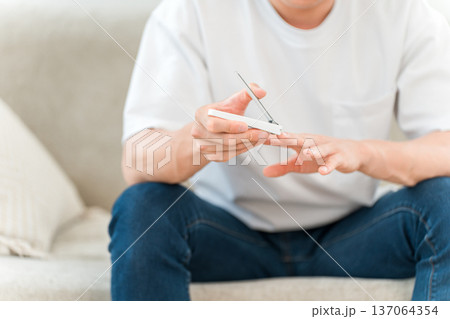 ソファに座り手の指の爪を切る若いアジア人男性 137064354