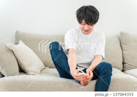 ソファに座り足の指の爪を切る若いアジア人男性 ソファに座り足の指の爪を切る若いアジア人男性 137064355