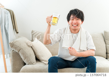 お風呂上がりにソファに座りジョッキでビールを飲む若いアジア人男性 137064718