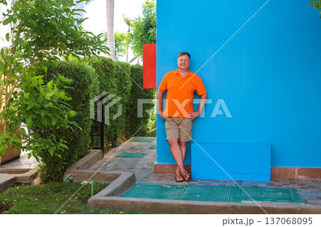 Portrait of an adult blond man against the blue wall of his house 137068095