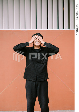 Young man covers his eyes with hands feeling overwhelmed Young man covers his eyes with hands feeling overwhelmed 137069539