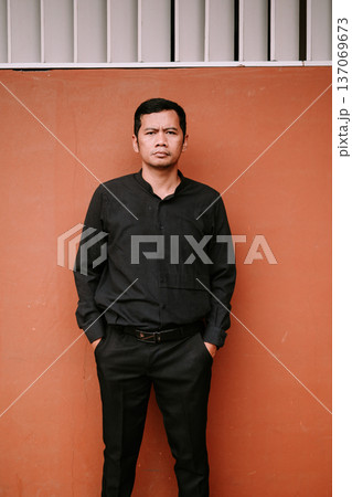 Confident Man in Black Shirt Standing Against Terracotta Wall 137069673