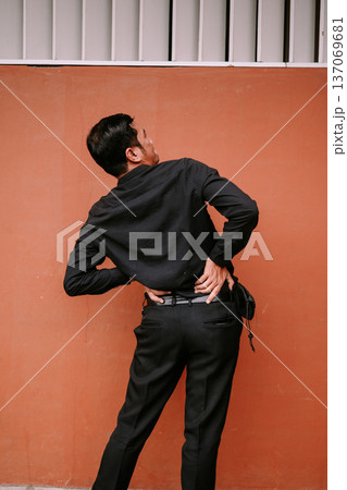 Young man experiencing lower back pain against orange wall 137069681