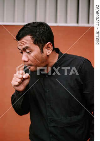 Young man coughing into his fist to prevent the spread of germs Young man coughing into his fist to prevent the spread of germs 137069692