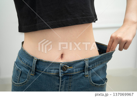 Young Asian woman losing weight wearing loose pants in oversize jeans. Young Asian woman losing weight wearing loose pants in oversize jeans. 137069967