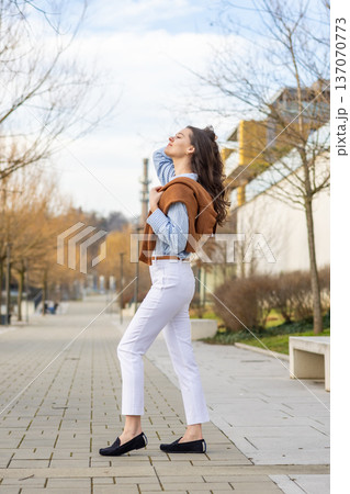 Elegant young woman in old money style walking along riverside promenade near pier in Prague during early spring. Understated luxury and timeless European lifestyle concept. Elegant young woman in old money style walking along riverside promenade near pier in Prague during early spring. Understated luxury and timeless European lifestyle concept. 137070773