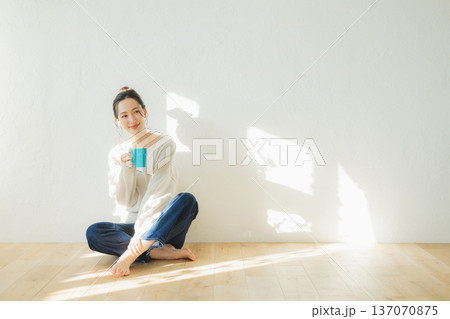 床に座ってコーヒーを飲む若い女性 床に座ってコーヒーを飲む若い女性 137070875